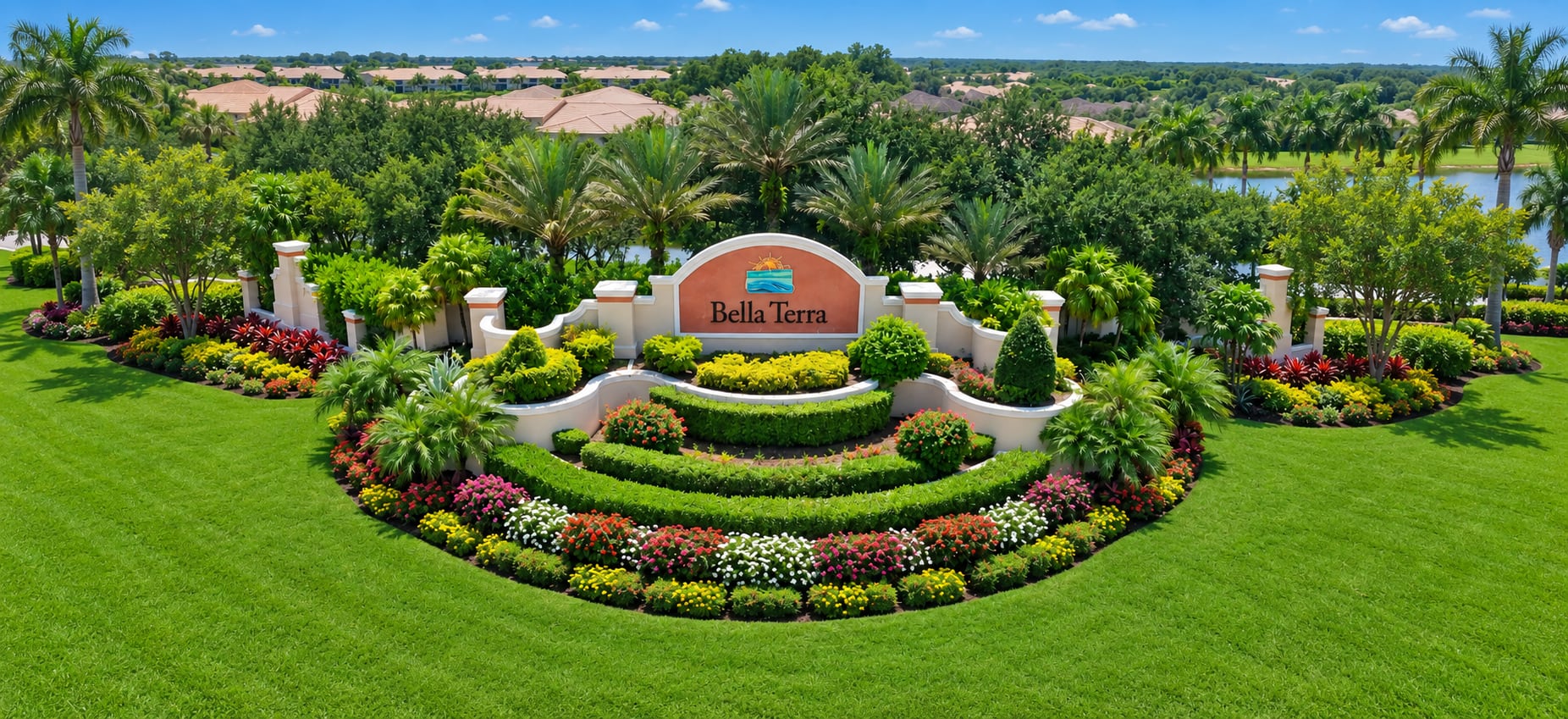The Bella Terra entrance sign in Estero, set in a curved formal garden of clipped hedges and flower beds, with palms and a lake behind