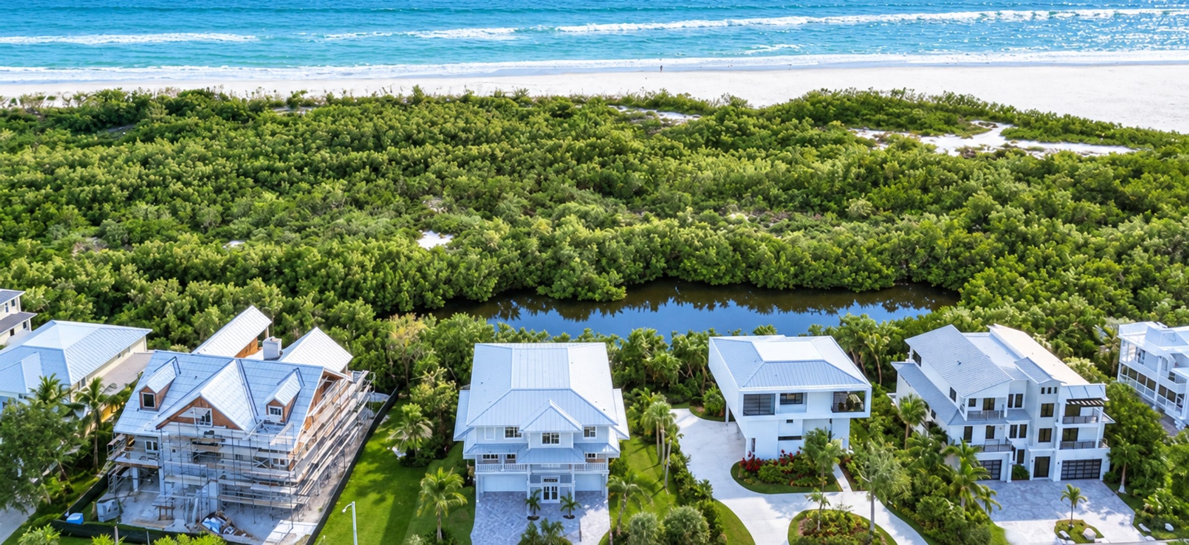 An aerial view of Hideaway Beach Club on Marco Island, Florida: houses set behind a tidal lagoon, with preserved mangrove and dune between them and a wide white beach on the Gulf, and no dock behind the homes.