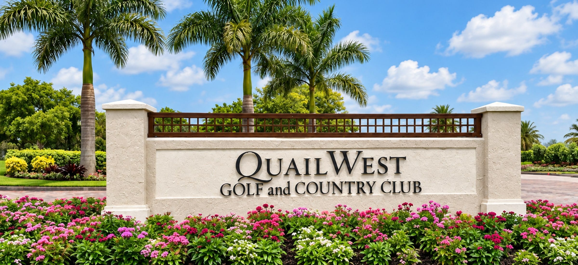 The Quail West Golf and Country Club entrance sign in Naples, Florida: black lettering on a long stucco monument under a timber lattice, with a bed of pink and white pentas across the front and royal palms behind.