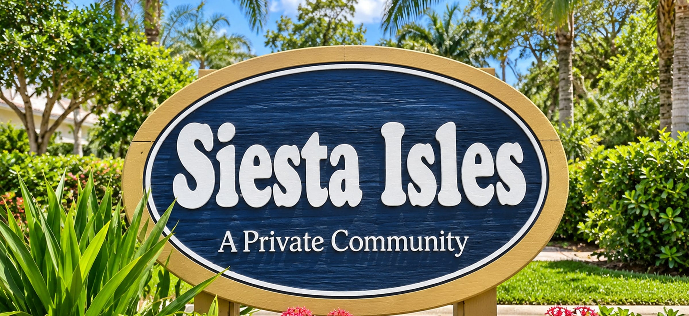The Siesta Isles entrance sign on Fort Myers Beach, Florida: an oval timber sign with a gold frame, the name in white on navy and the words A Private Community beneath it, set in a clipped hedge with red ixora in flower and palms behind.